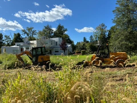An excavator and compact loader on an overgrown lot near Princeton in late summer.