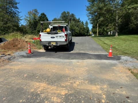 A fresh asphalt patch across a driveway where a utility trench was cut and rebuilt.