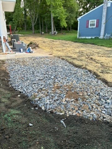 A bed of clean drainage stone installed along the edge of a patio and lawn.