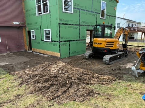 A mini excavator and skid steer grading bare soil beside a home under construction, ground worked smooth around the foundation.