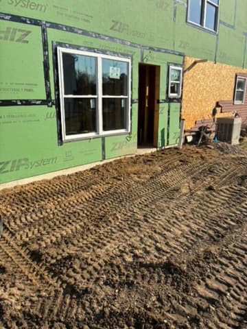 Freshly graded, track-marked soil worked smooth right up to a home's foundation, ready for finish work.