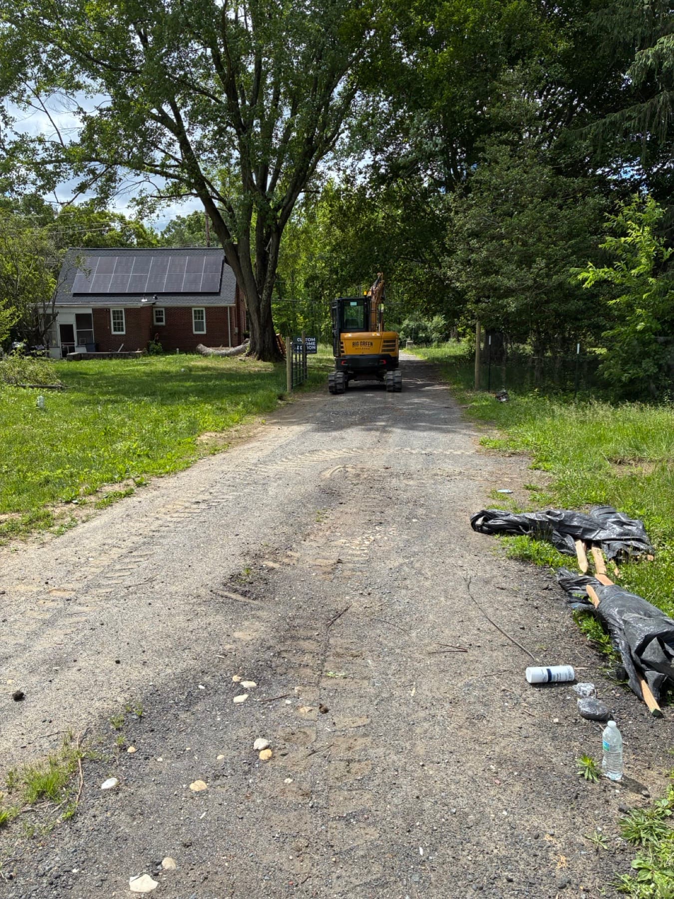 A compact mini excavator working in a residential side yard, with the lawn and plantings around the work area protected.